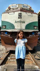 Girl Standing on Train Tracks in Front of Amtrak Train